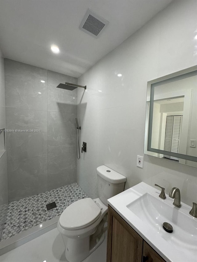 full bath with vanity, toilet, visible vents, and tiled shower