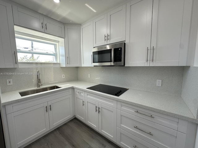 kitchen with a sink, stainless steel microwave, black electric stovetop, and white cabinets