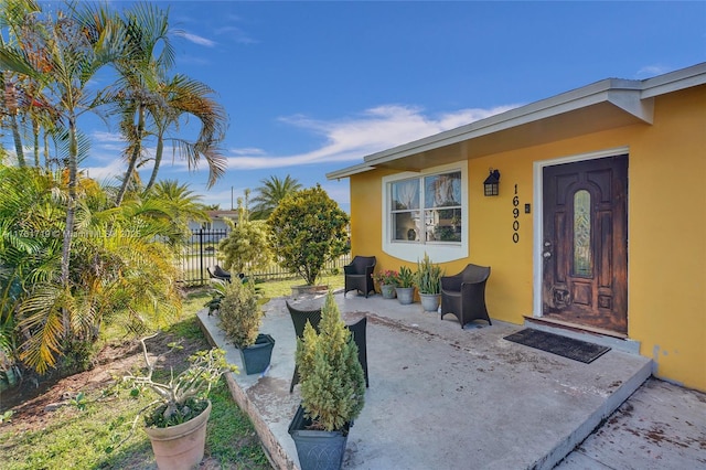 view of exterior entry featuring a patio area, stucco siding, and fence