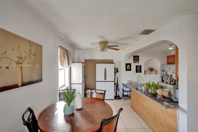 dining area with a ceiling fan, visible vents, light tile patterned flooring, arched walkways, and a textured ceiling