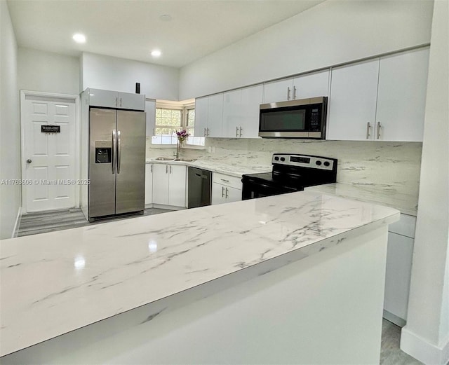 kitchen with a sink, white cabinetry, appliances with stainless steel finishes, decorative backsplash, and light stone countertops