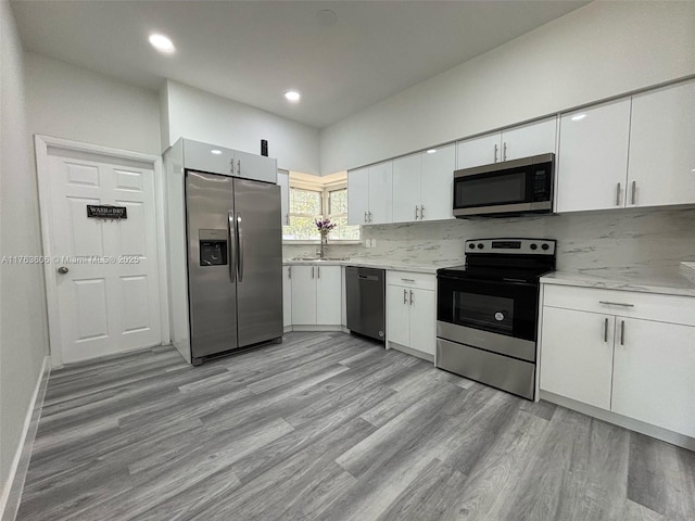 kitchen featuring light wood finished floors, a sink, stainless steel appliances, white cabinetry, and tasteful backsplash