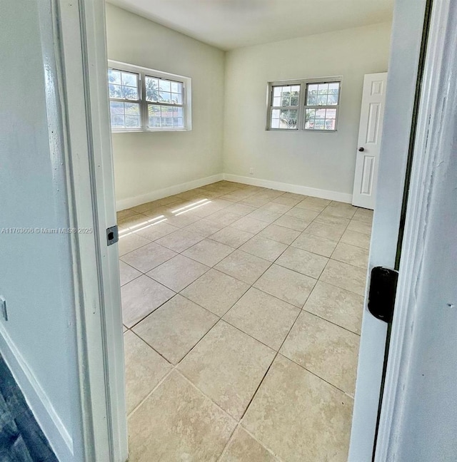 unfurnished room with light tile patterned floors, a healthy amount of sunlight, and baseboards