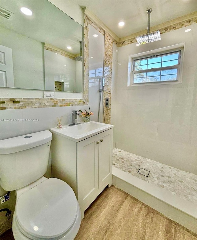 bathroom featuring toilet, tiled shower, tile walls, and wood finished floors