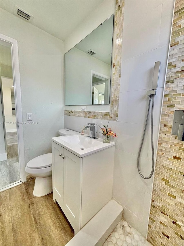 bathroom featuring visible vents, toilet, a tile shower, wood finished floors, and vanity