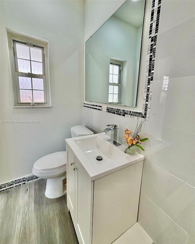 half bath with vanity, toilet, wood finished floors, and baseboard heating