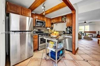 kitchen featuring beam ceiling, brown cabinets, a ceiling fan, stainless steel appliances, and light tile patterned floors