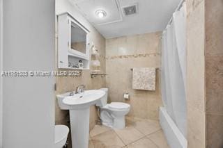 bathroom featuring tile patterned floors, toilet, and tile walls