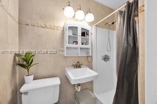 bathroom featuring a notable chandelier, toilet, a shower with shower curtain, and a sink