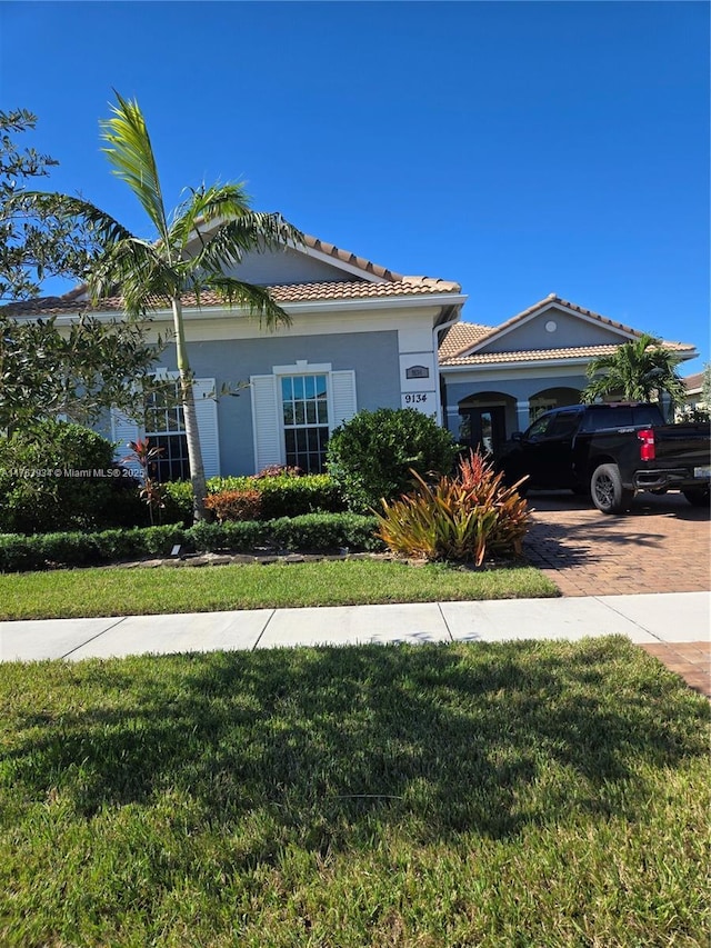 view of front of house with a front yard, a tiled roof, decorative driveway, and stucco siding