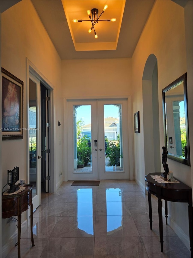 entrance foyer with a tray ceiling, french doors, arched walkways, and plenty of natural light