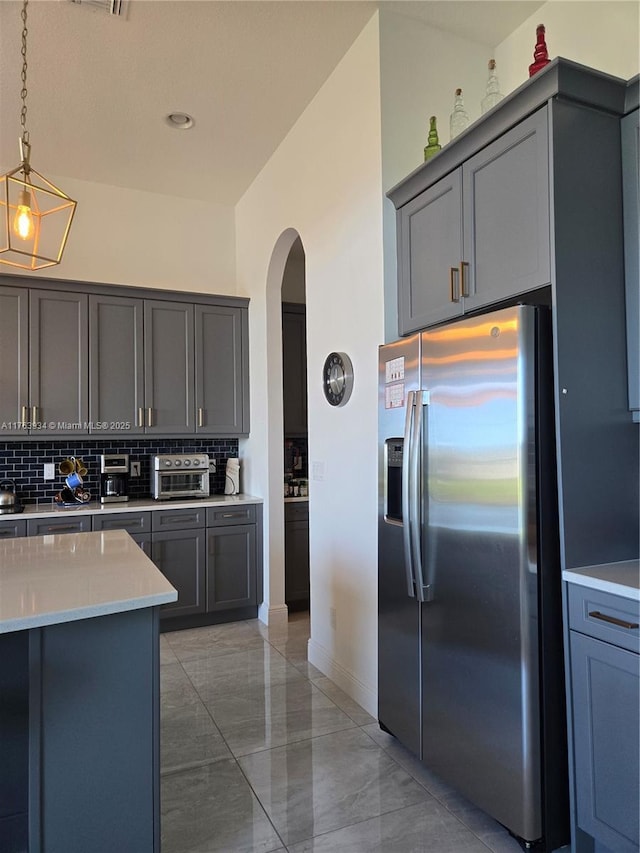 kitchen featuring decorative backsplash, arched walkways, stainless steel fridge, and gray cabinetry