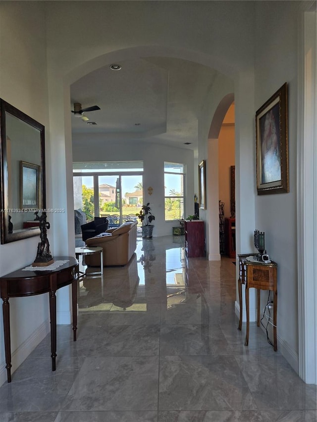 hallway featuring baseboards, arched walkways, and marble finish floor