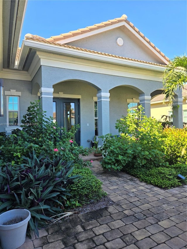 view of exterior entry with brick siding, stucco siding, and a tile roof