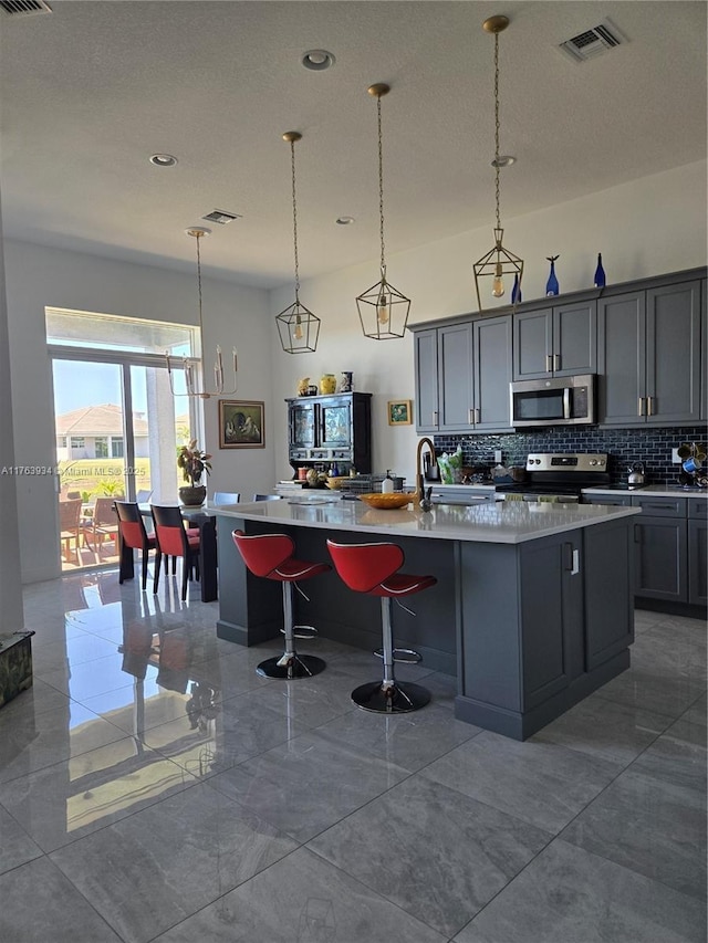 kitchen with visible vents, backsplash, appliances with stainless steel finishes, and an island with sink