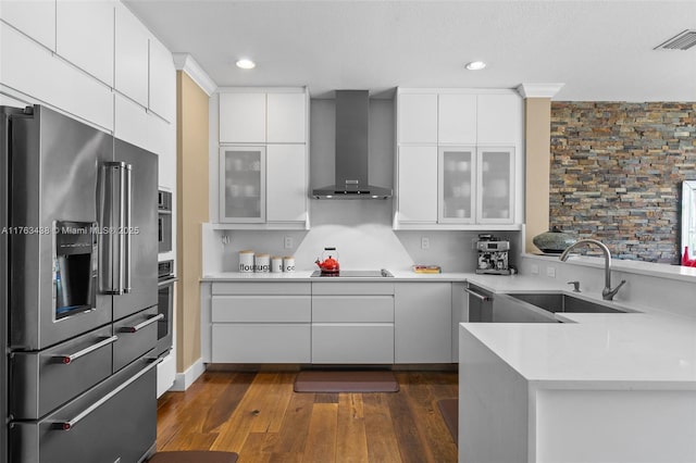 kitchen featuring visible vents, glass insert cabinets, wall chimney range hood, appliances with stainless steel finishes, and a sink