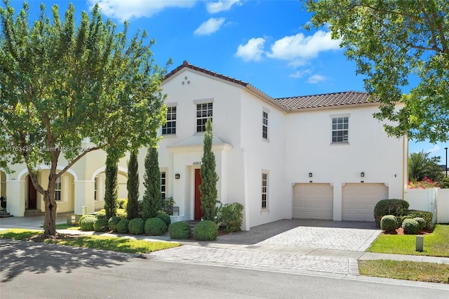 mediterranean / spanish-style house with fence, a tiled roof, stucco siding, decorative driveway, and an attached garage