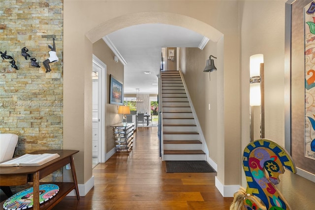 foyer entrance featuring stairway, wood finished floors, arched walkways, and ornamental molding