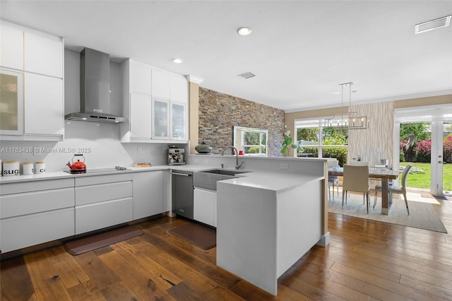 kitchen featuring a sink, light countertops, a peninsula, wall chimney exhaust hood, and stainless steel dishwasher