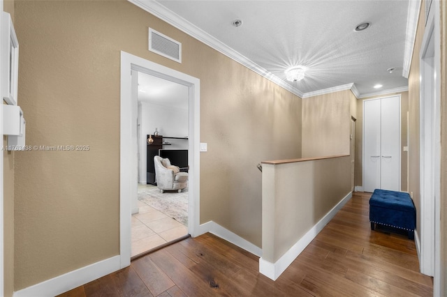 hall with visible vents, baseboards, ornamental molding, and hardwood / wood-style flooring