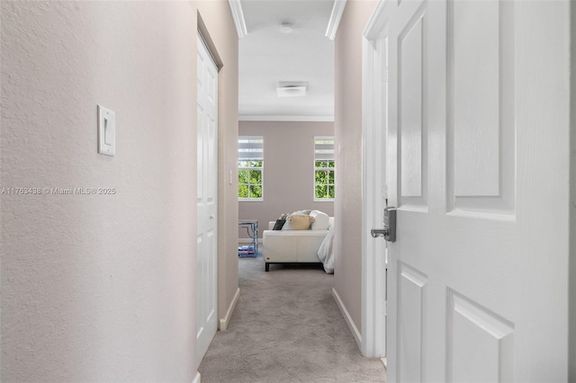 hall with baseboards, light colored carpet, crown molding, and a textured wall