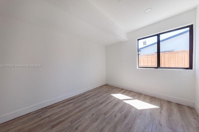 empty room with beamed ceiling, baseboards, and wood finished floors