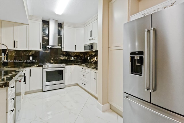 kitchen featuring marble finish floor, backsplash, white cabinetry, appliances with stainless steel finishes, and wall chimney exhaust hood