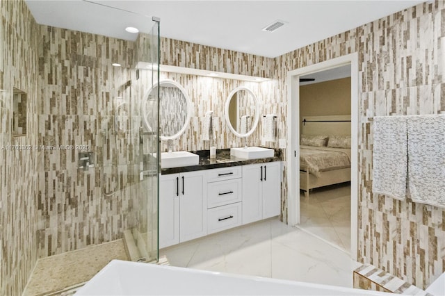 full bathroom with visible vents, wallpapered walls, double vanity, a tile shower, and connected bathroom