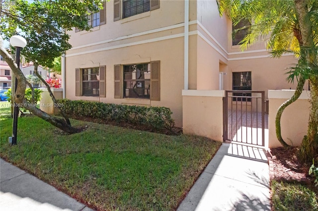 view of side of property with a gate, a lawn, fence, and stucco siding