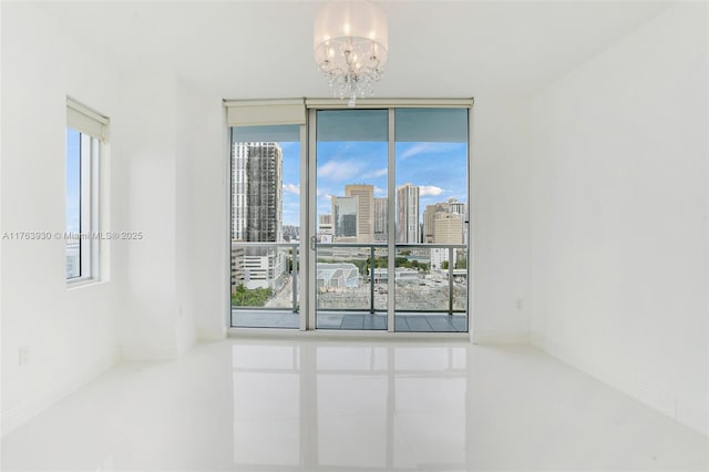empty room with an inviting chandelier, a view of city, baseboards, and expansive windows