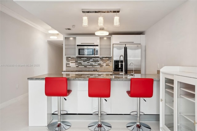 kitchen with a kitchen bar, visible vents, tasteful backsplash, glass insert cabinets, and stainless steel appliances
