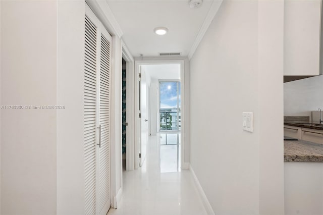 hallway with visible vents, crown molding, baseboards, floor to ceiling windows, and a sink