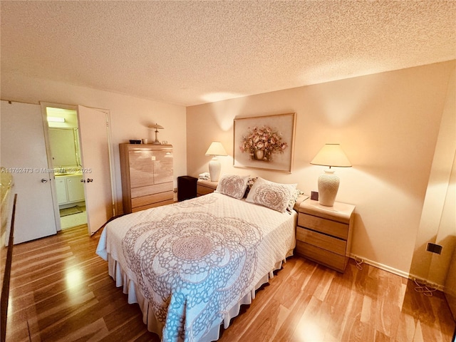 bedroom featuring baseboards, a textured ceiling, wood finished floors, and ensuite bathroom