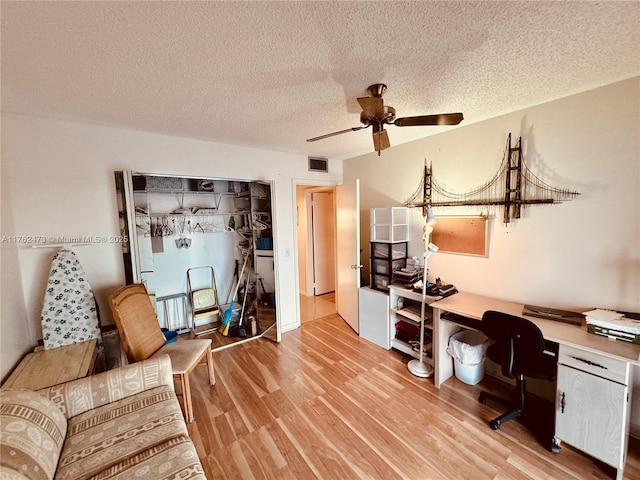 home office with a textured ceiling, visible vents, light wood finished floors, and ceiling fan