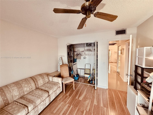 living area featuring a textured ceiling, wood finished floors, visible vents, and ceiling fan