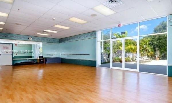 interior space with a drop ceiling, floor to ceiling windows, visible vents, and wood finished floors