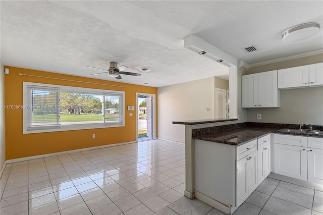 kitchen with visible vents, a sink, a peninsula, white cabinets, and light tile patterned floors