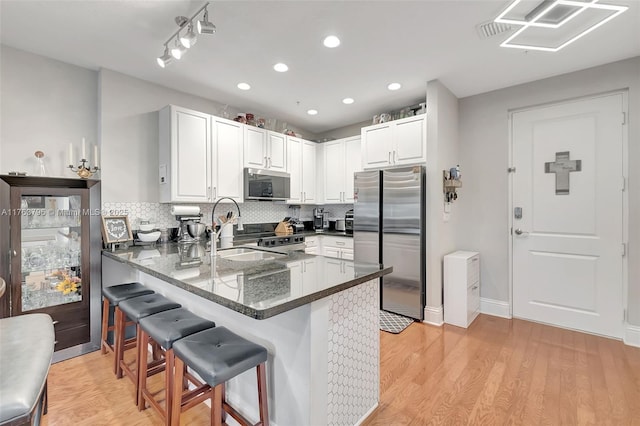 kitchen featuring light wood-style flooring, a sink, a kitchen breakfast bar, appliances with stainless steel finishes, and a peninsula