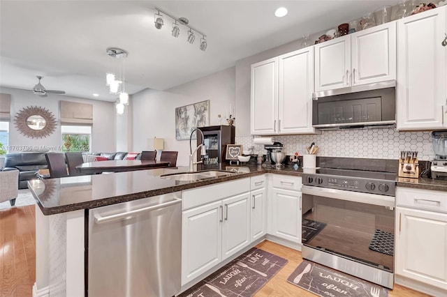 kitchen featuring a sink, stainless steel appliances, a peninsula, light wood finished floors, and decorative backsplash