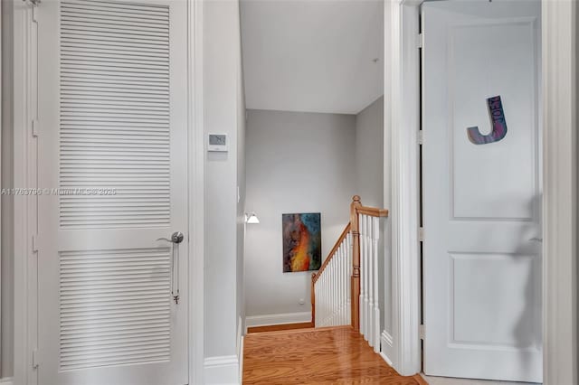 hall featuring an upstairs landing, light wood-type flooring, and baseboards