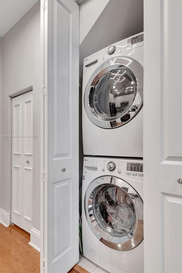 laundry area featuring laundry area, stacked washer and clothes dryer, and light wood-type flooring