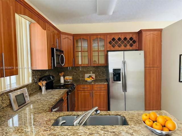 kitchen featuring light stone counters, glass insert cabinets, appliances with stainless steel finishes, and a sink