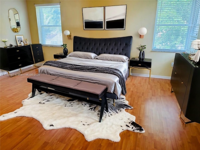 bedroom with multiple windows, wood finished floors, and baseboards