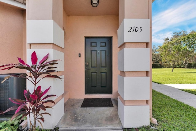 entrance to property featuring stucco siding, central air condition unit, and a yard