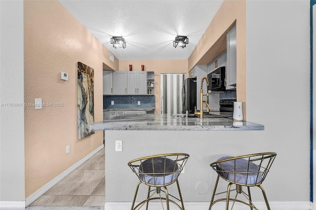 kitchen with baseboards, light stone countertops, a breakfast bar, a peninsula, and black appliances