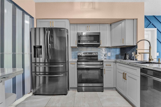 kitchen featuring tasteful backsplash, stainless steel appliances, light stone counters, and a sink