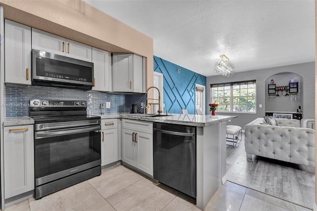 kitchen featuring open floor plan, decorative backsplash, a peninsula, stainless steel appliances, and a sink