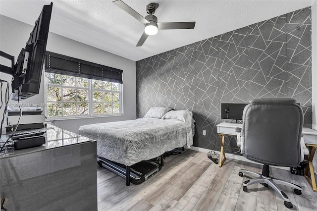 bedroom with a ceiling fan, a textured ceiling, wood finished floors, baseboards, and an accent wall