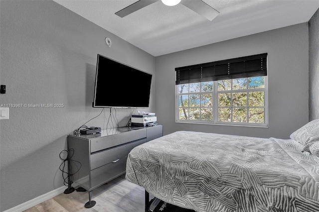 bedroom with baseboards, ceiling fan, light wood-style flooring, a textured wall, and a textured ceiling