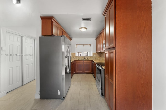 kitchen featuring visible vents, backsplash, brown cabinetry, stainless steel appliances, and a sink